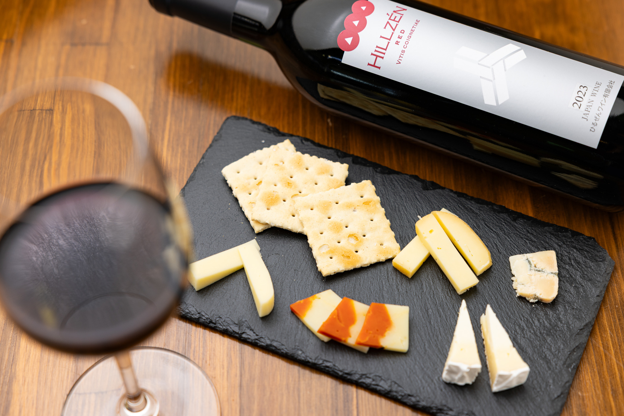 「山葡萄-赤」グラス大850円と「チーズ盛り合わせ」800円。チーズは、「蒜山酪農農業協同組合」によるゴーダチーズ・カマンベールチーズ、「蒜山ラッテバンビーノ」のブルーチーズ・チェダーチーズなどがセットに